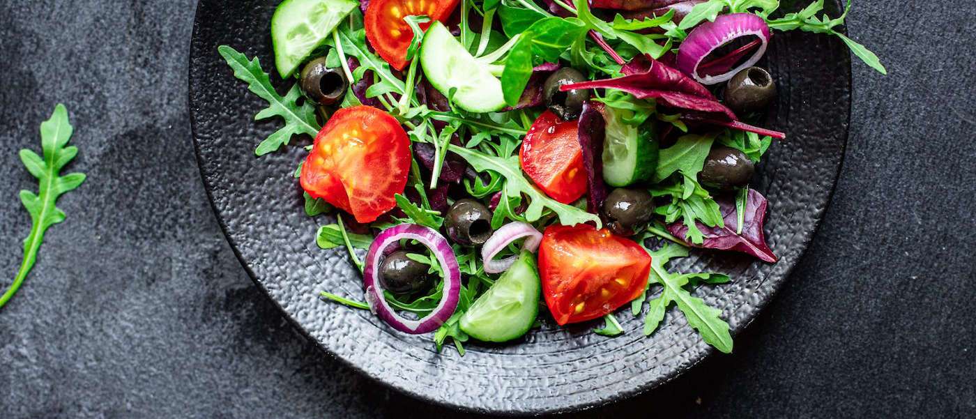 une salade avec des tomates, de la laitue et des olives sur une assiette.