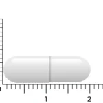 Une seule capsule blanche de Vitakruid – Zinc Méthionine & Cuivre (90 capsules végétales) est présentée à côté d’une règle, mesurant environ 2 centimètres de long.